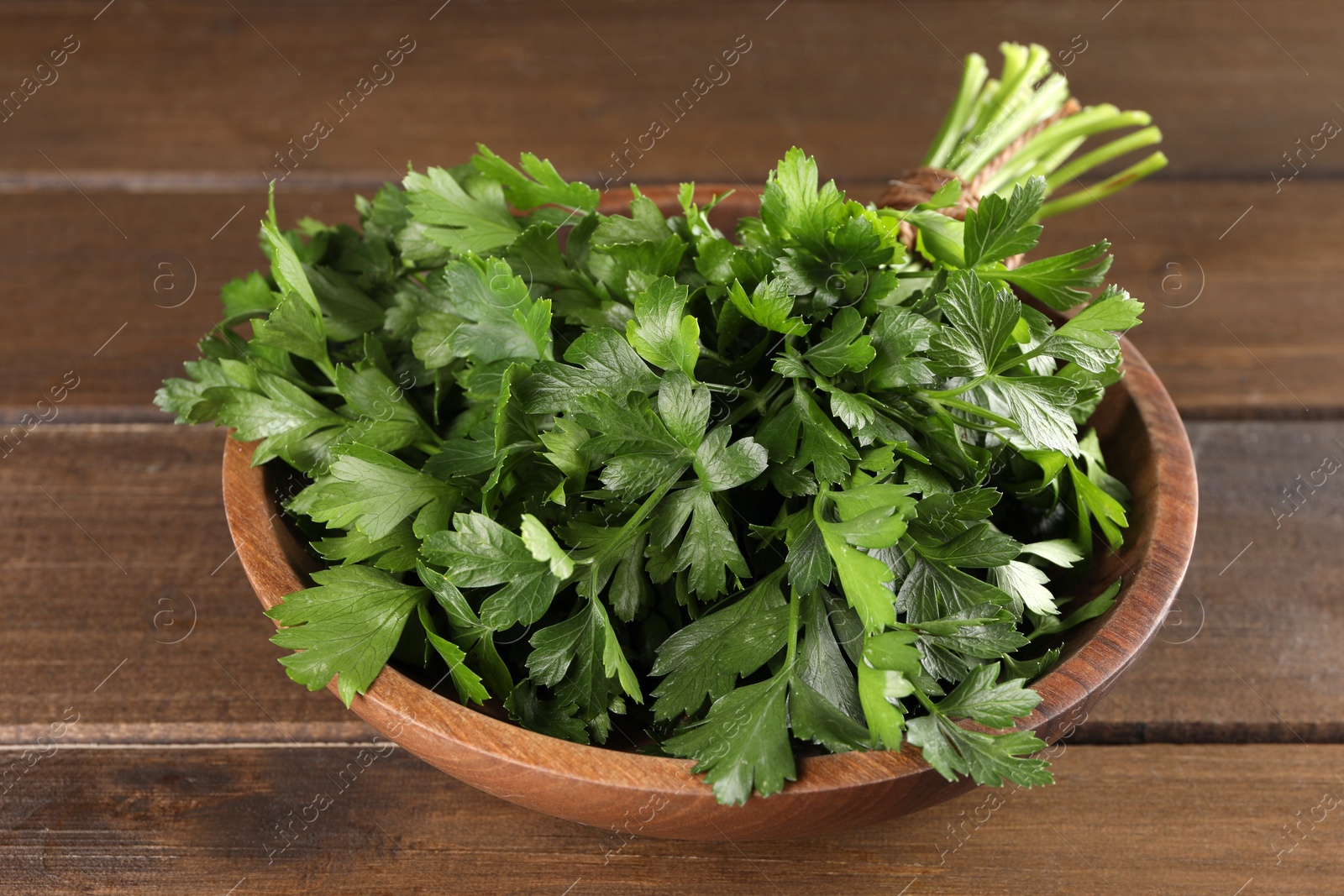 Photo of Bunch of fresh parsley in bowl on wooden table, closeup