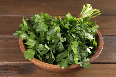 Photo of Bunch of fresh parsley in bowl on wooden table, closeup