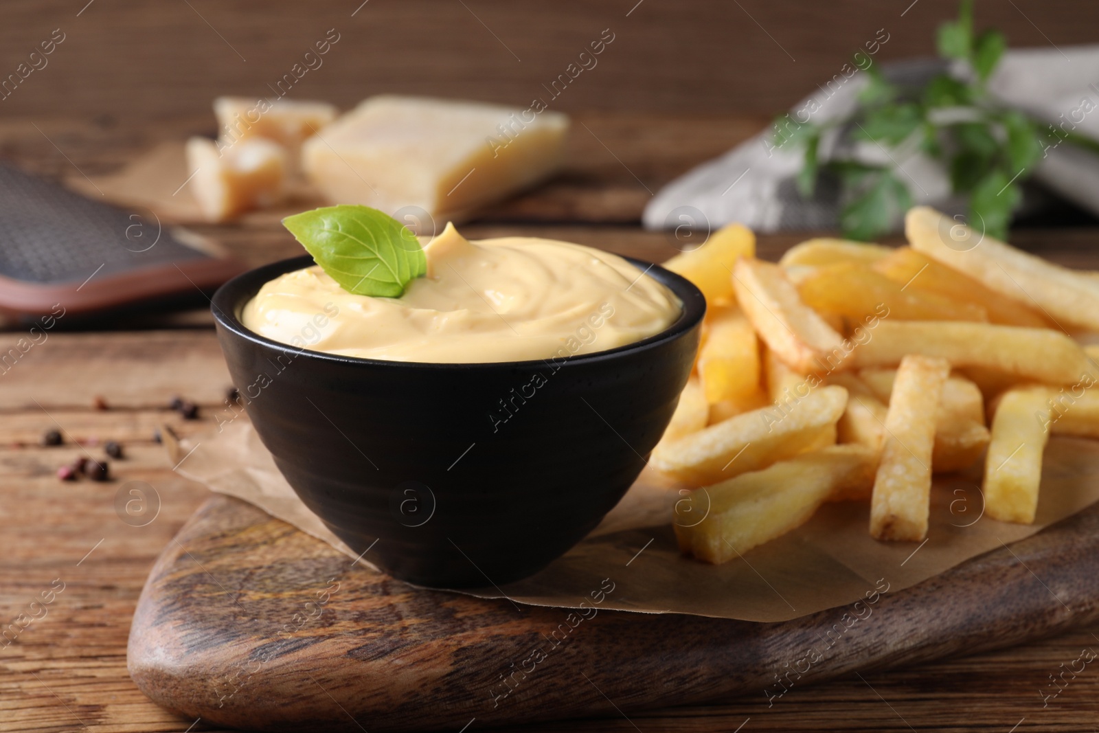 Photo of Delicious French fries and cheese sauce with basil on wooden table, closeup