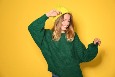 Image of Happy young woman wearing warm sweater and knitted hat on yellow background 