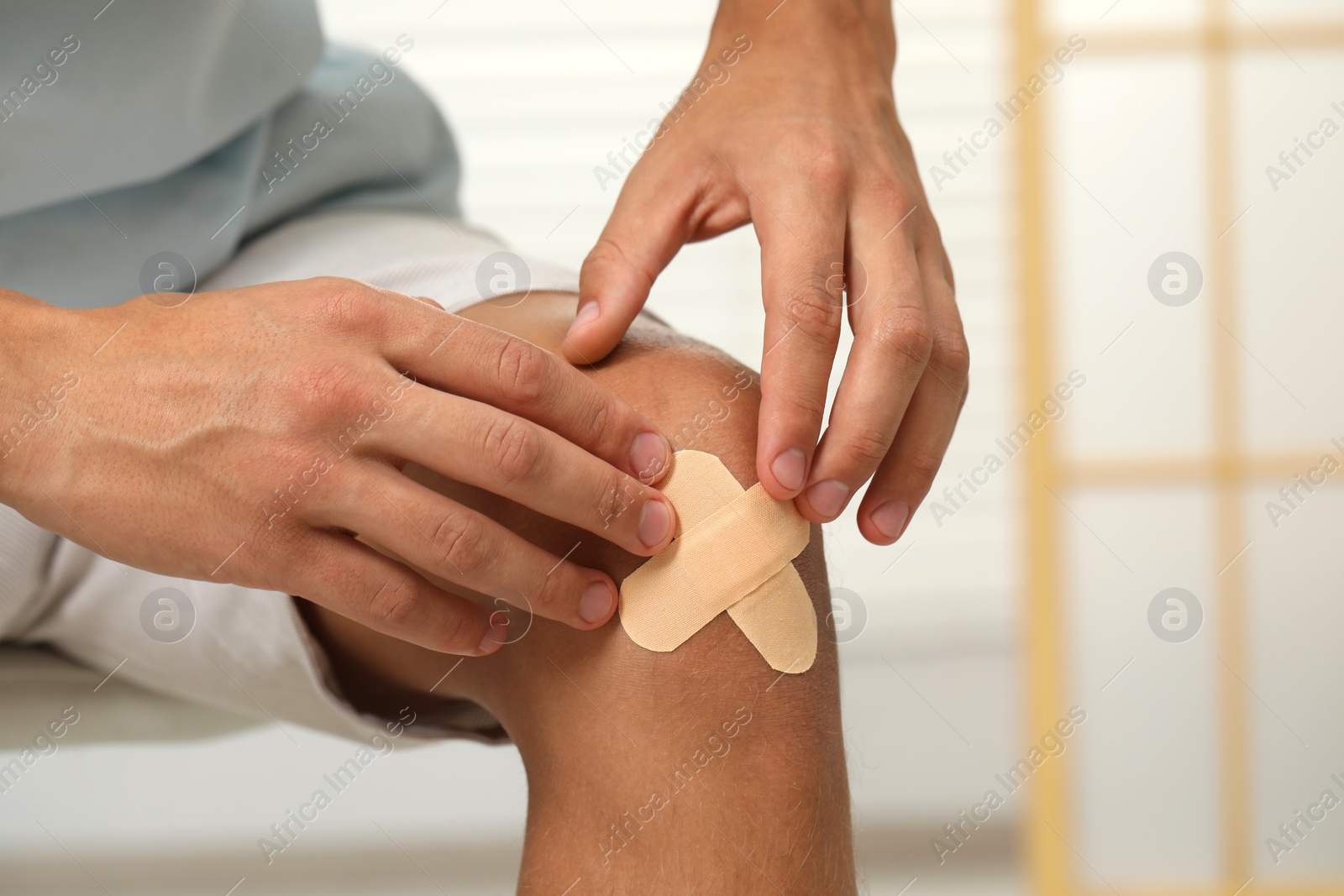 Photo of Man putting sticking plasters onto knee indoors, closeup