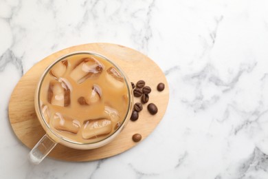 Photo of Refreshing iced coffee with milk in glass cup and beans on white marble table, top view. Space for text