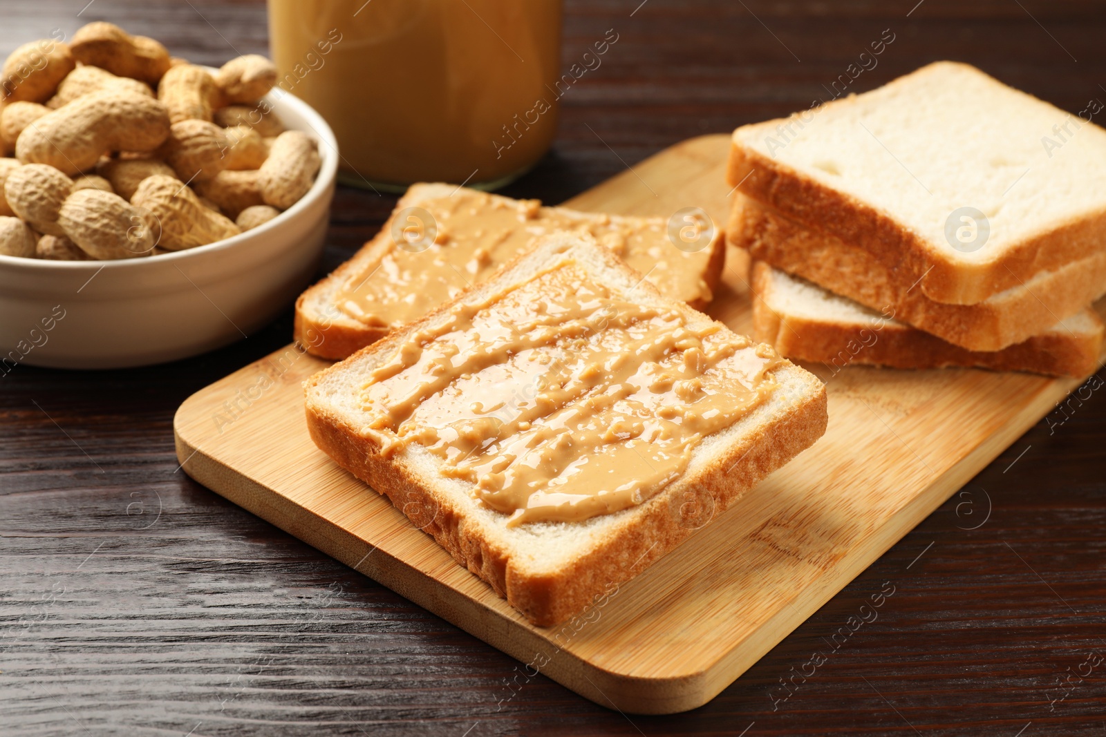 Photo of Delicious toasts with peanut butter and nuts on wooden table, closeup