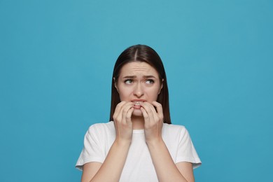 Young woman biting her nails on light blue background