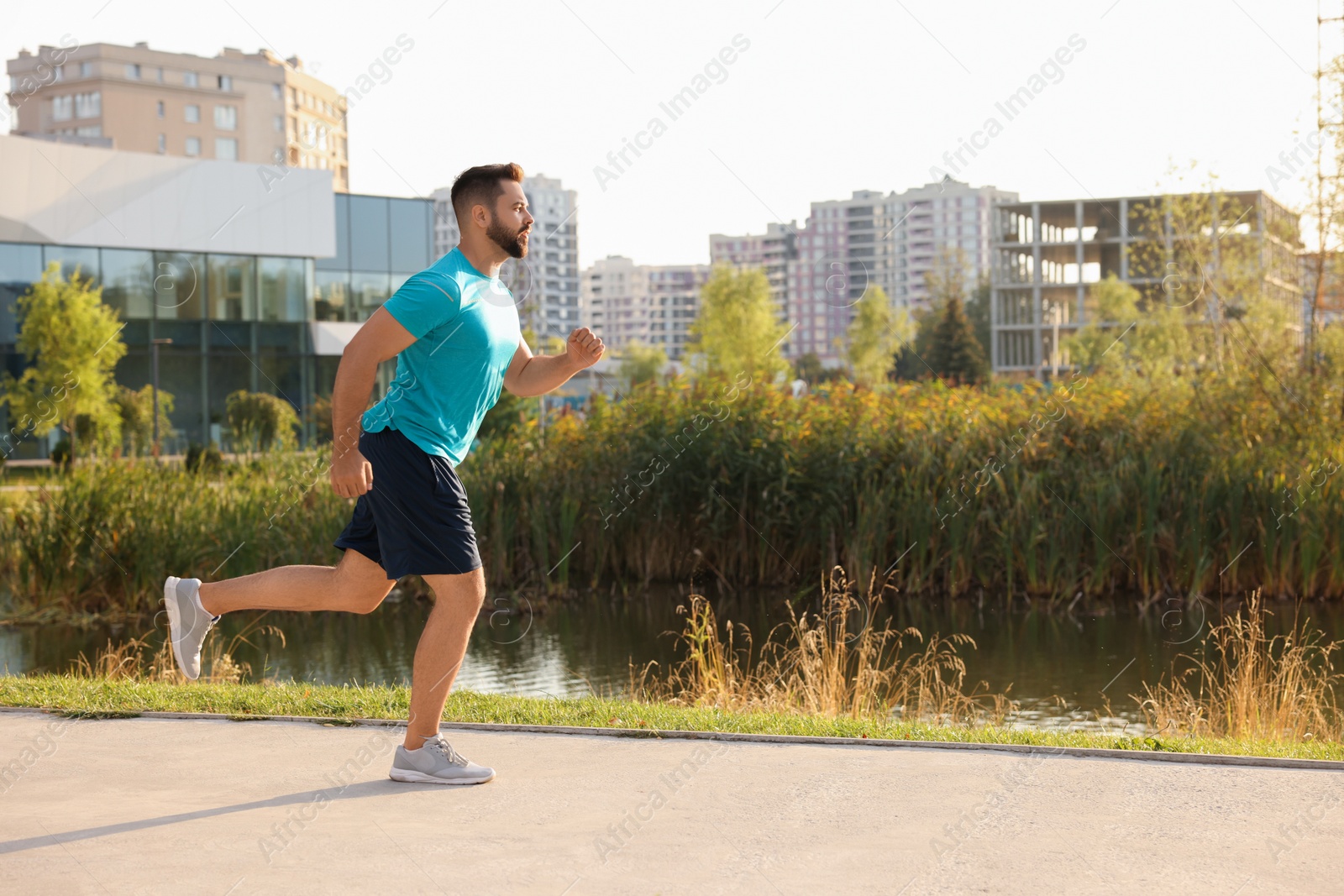 Photo of Young man running near pond in park. Space for text