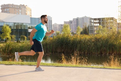 Young man running near pond in park. Space for text