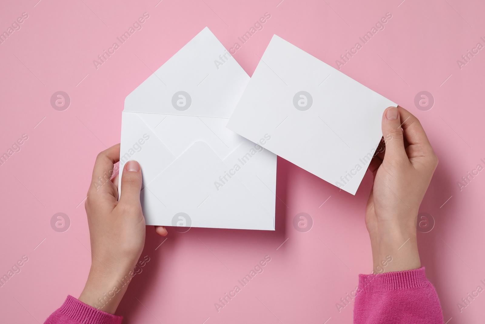 Photo of Woman with blank card and letter envelope at pink table, top view. Space for text