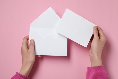 Photo of Woman with blank card and letter envelope at pink table, top view. Space for text