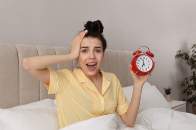 Photo of Emotional overslept woman with alarm clock in bed. Being late concept