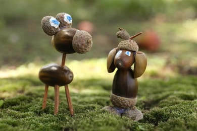 Photo of Cute figures made of acorns on green moss outdoors, closeup
