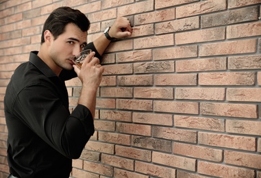 Young man with glass of whiskey near brick wall indoors. Space for text