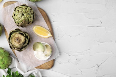 Delicious cooked artichokes with tasty sauce served on white textured table, flat lay. Space for text