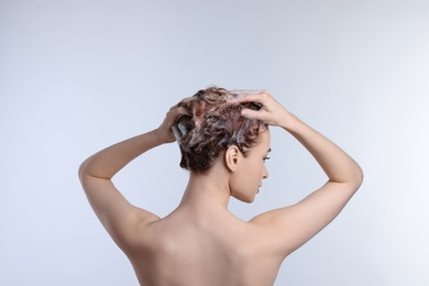 Photo of Young woman washing her hair with shampoo on light grey background, back view