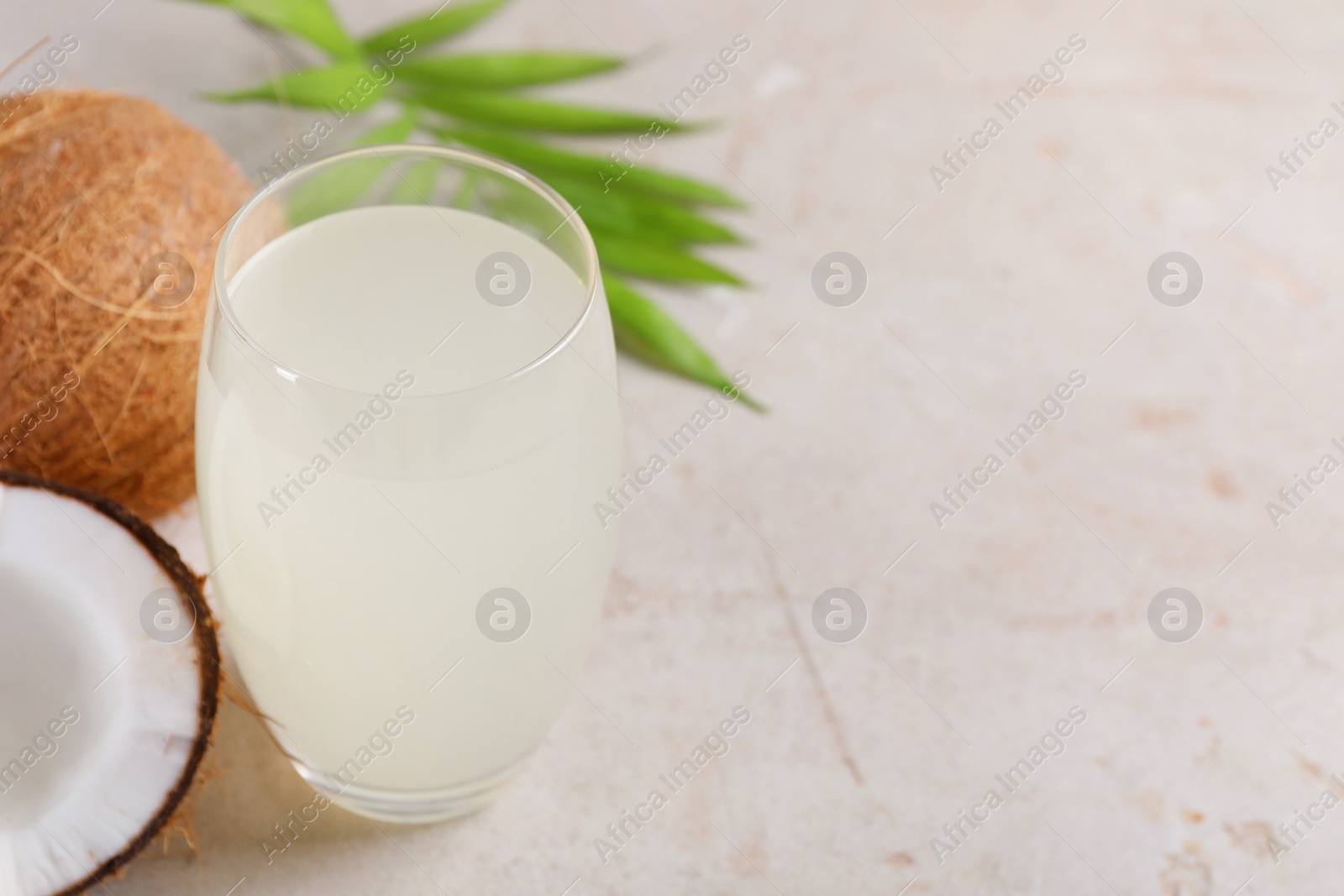 Photo of Glass of coconut water, palm leaves and nuts on light table. Space for text