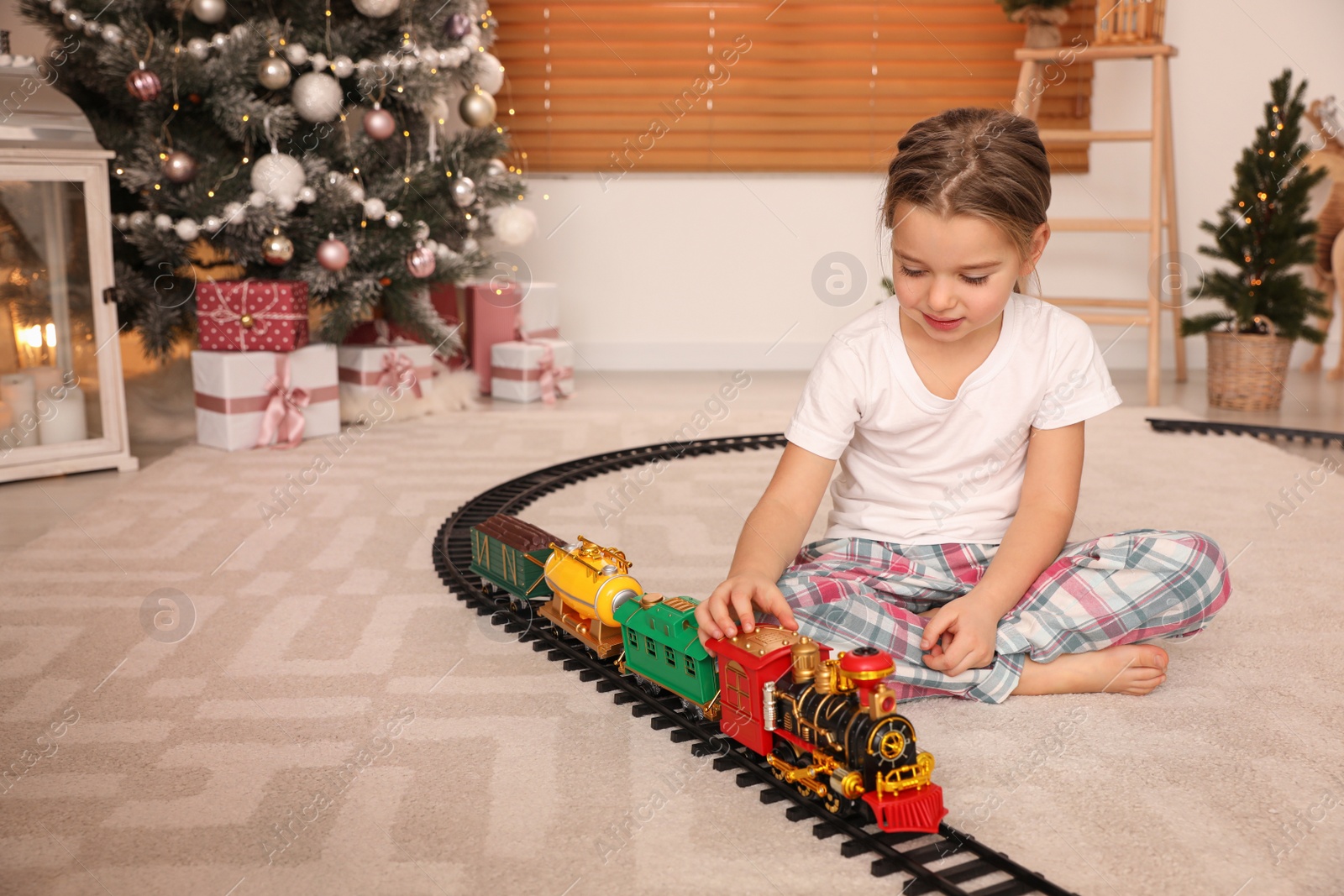 Photo of Little girl playing with colorful train toy in room decorated for Christmas