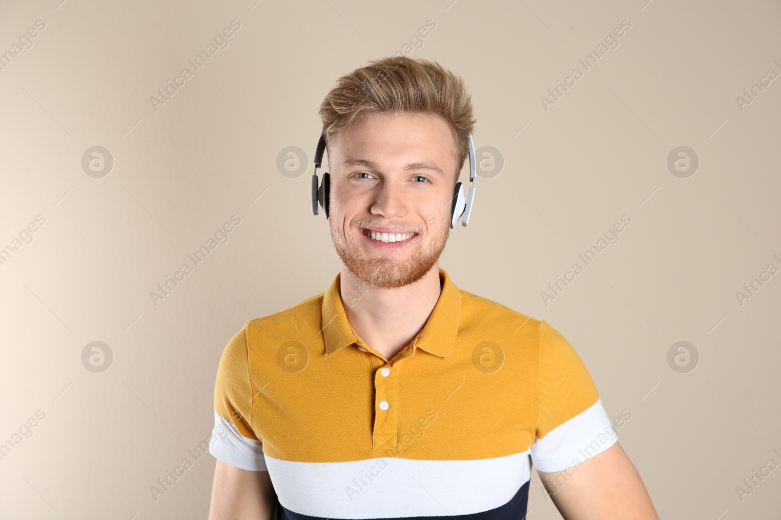 Photo of Handsome young man listening to music with headphones on color background