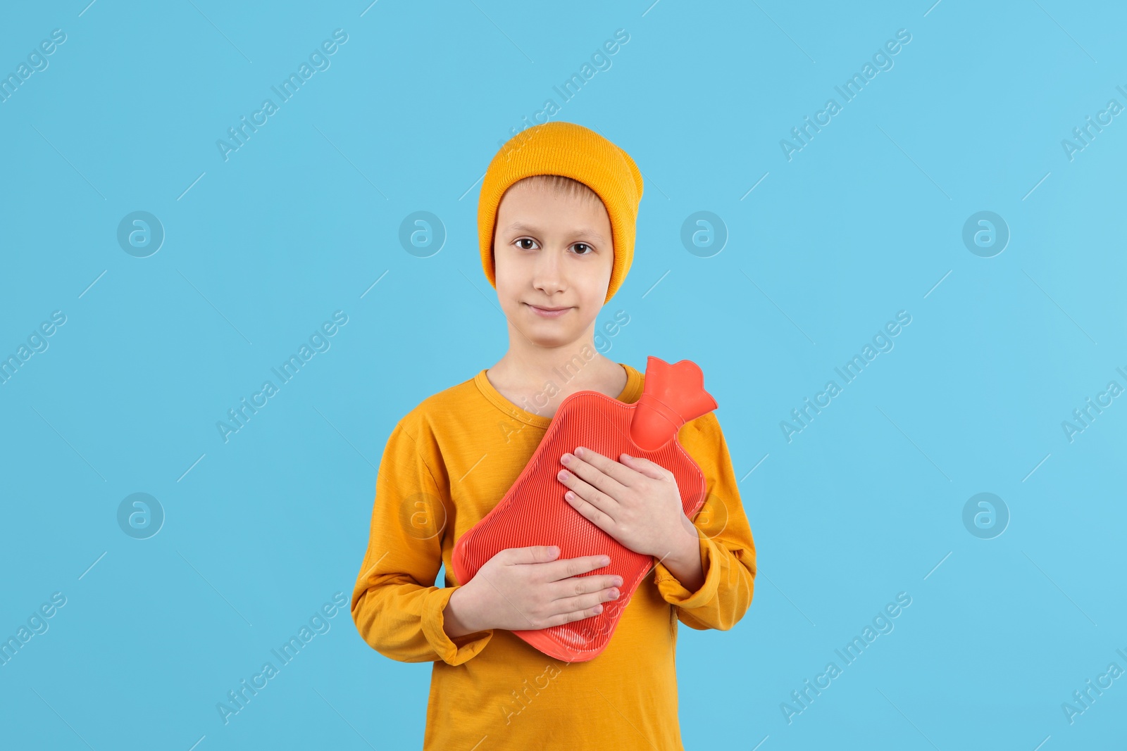 Photo of Ill boy with hot water bottle suffering from cold on light blue background