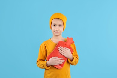 Photo of Ill boy with hot water bottle suffering from cold on light blue background