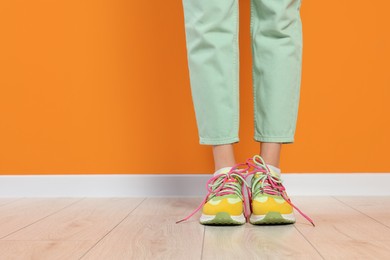 Woman wearing pair of new stylish sneakers near orange wall, closeup. Space for text