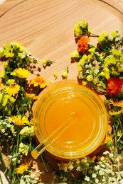 Delicious fresh honey in glass jar and beautiful flowers on wooden board, flat lay