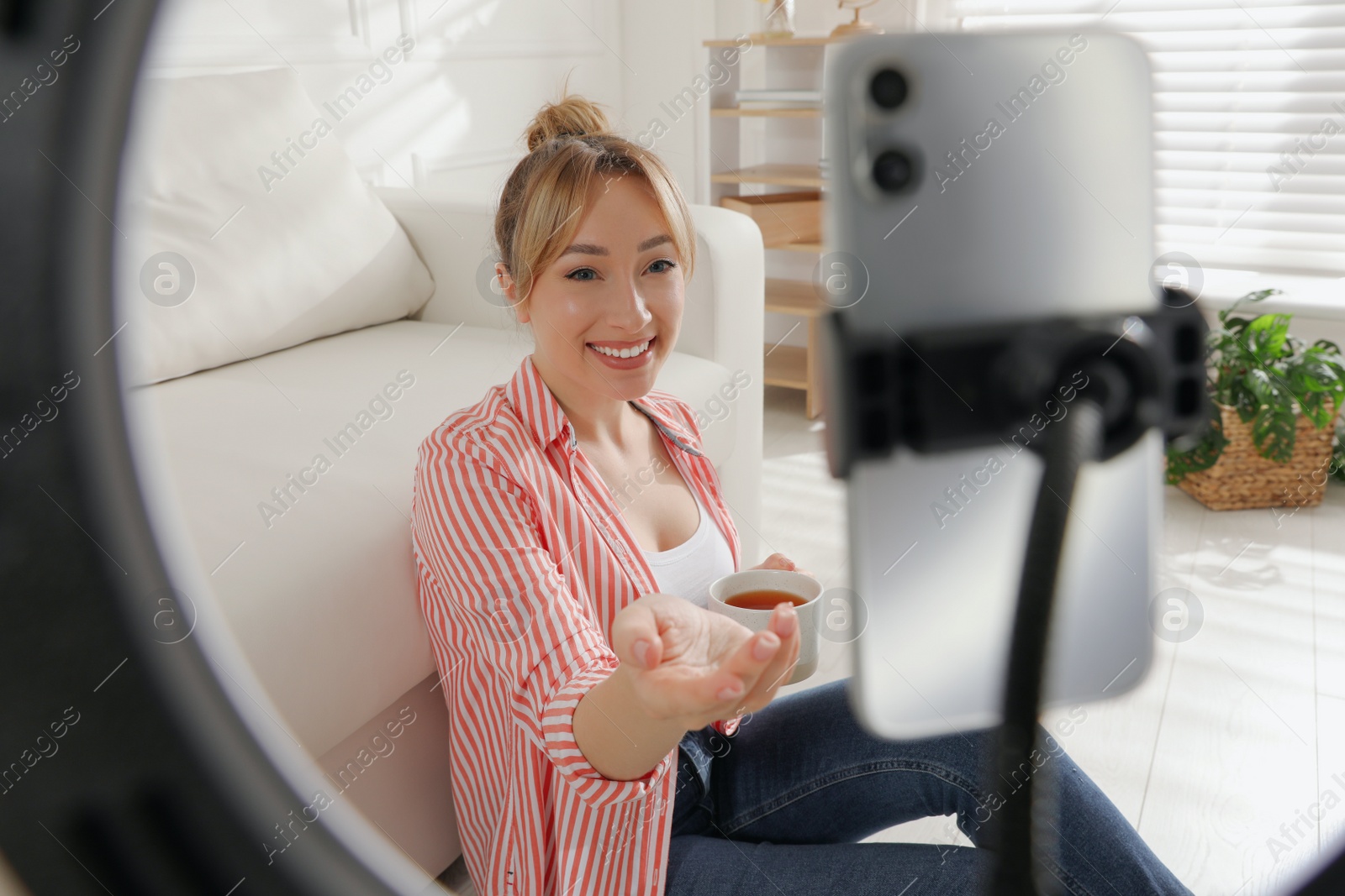 Photo of Blogger with cup of tea recording video at home, view through ring lamp