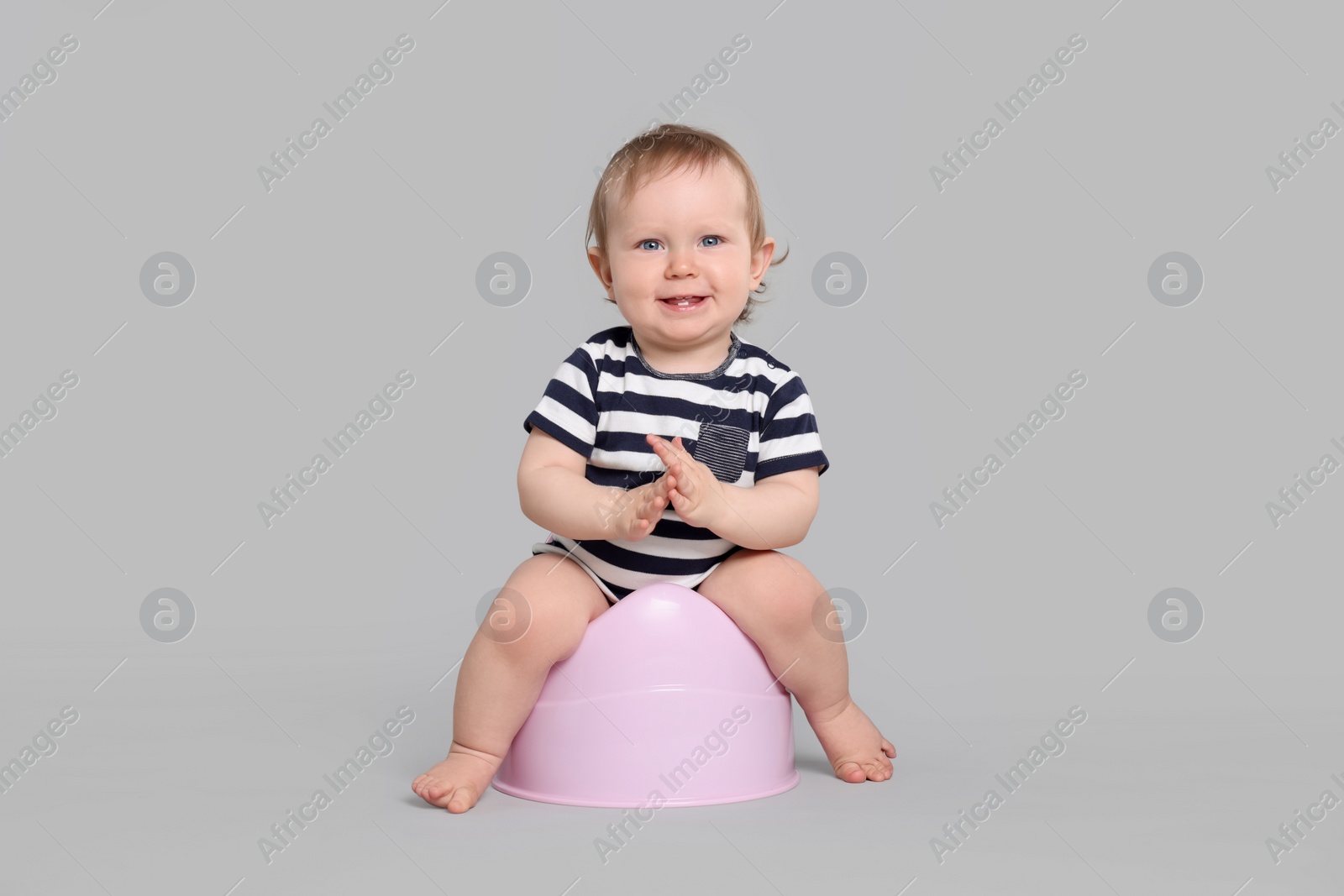 Photo of Little child sitting on baby potty against light grey background