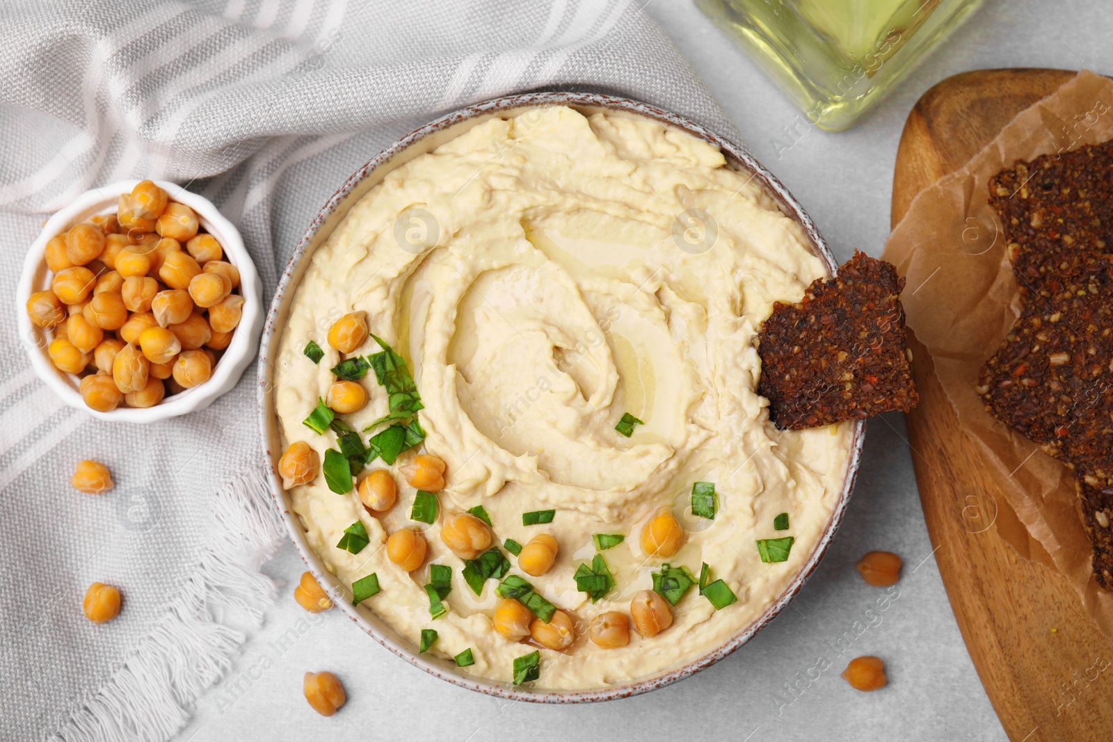 Photo of Delicious hummus with chickpeas and crispbread served on light grey table, flat lay