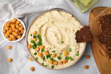 Delicious hummus with chickpeas and crispbread served on light grey table, flat lay