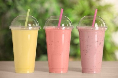 Photo of Plastic cups with different tasty smoothies on wooden table outdoors