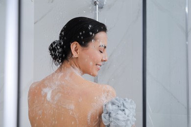 Young woman with mesh pouf taking shower at home