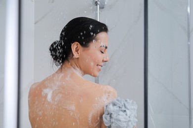 Photo of Young woman with mesh pouf taking shower at home