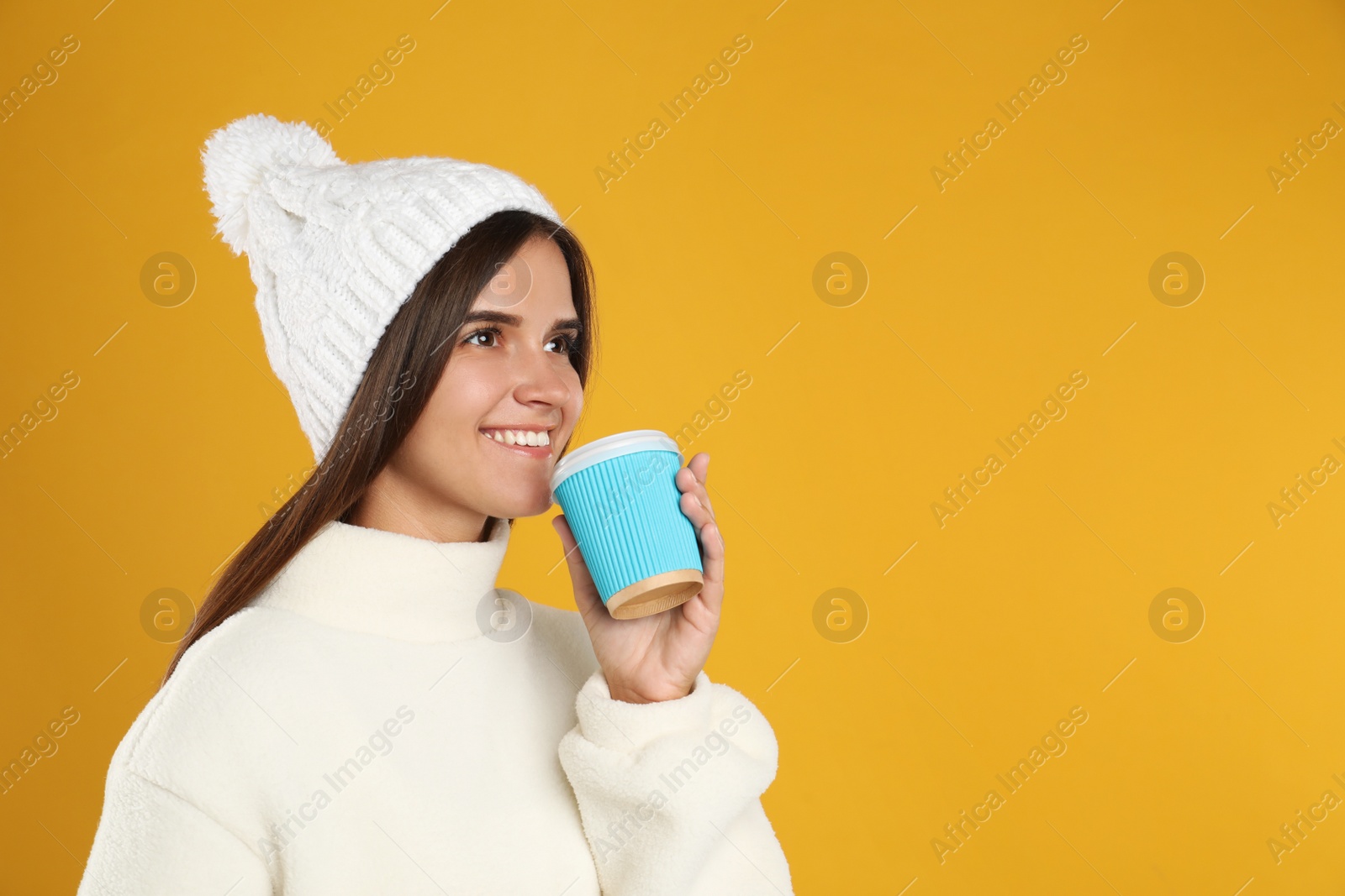 Photo of Happy beautiful woman with paper cup of mulled wine on yellow background. Space for text