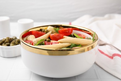 Tasty baby corn with tomatoes, arugula and capers on white tiled table, closeup