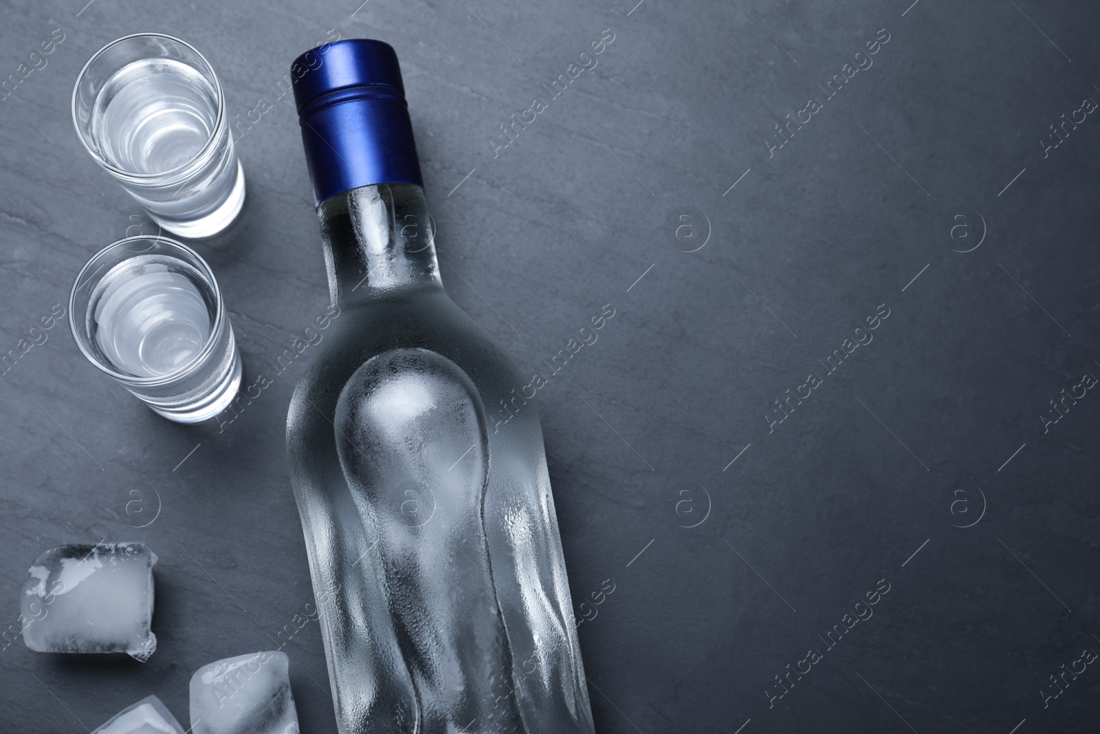 Photo of Bottle of vodka, ice cubes and shot glasses on black table, flat lay. Space for text