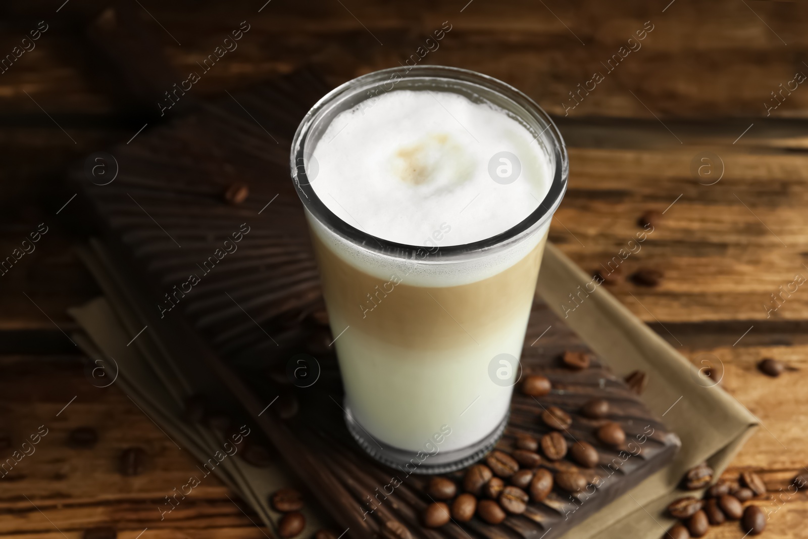 Photo of Delicious latte macchiato and coffee beans on wooden table