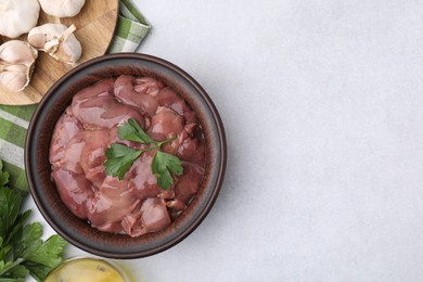 Bowl with raw chicken liver, parsley and garlic on white table, flat lay. Space for text