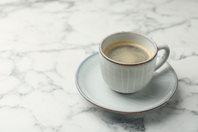 Tasty coffee in cup and saucer on white marble table, closeup. Space for text