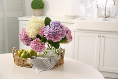 Photo of Bouquet of beautiful hydrangea flowers and apples on table in kitchen, space for text. Interior design