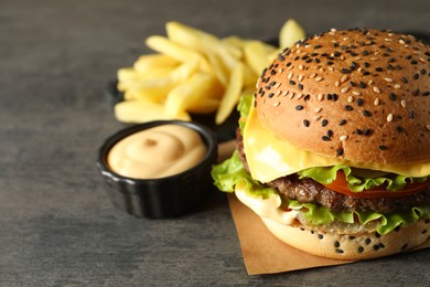 Photo of Burger with delicious patty, french fries and sauce on gray table
