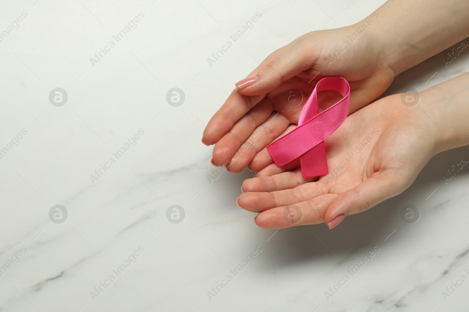 Photo of Breast cancer awareness. Woman with pink ribbon at white marble table, top view. Space for text
