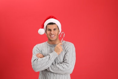Photo of Handsome man in Santa hat holding candy cane on red background