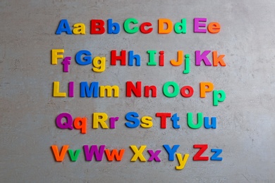 Colorful magnetic letters on grey stone background, flat lay. Alphabetical order