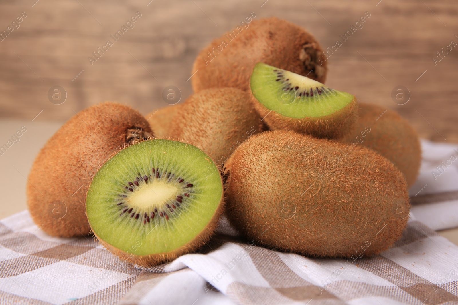 Photo of Heap of whole and cut fresh kiwis on checkered tablecloth, closeup