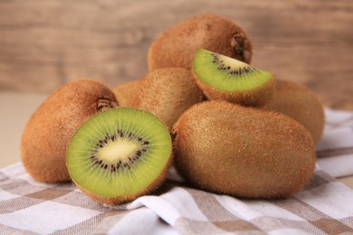 Heap of whole and cut fresh kiwis on checkered tablecloth, closeup