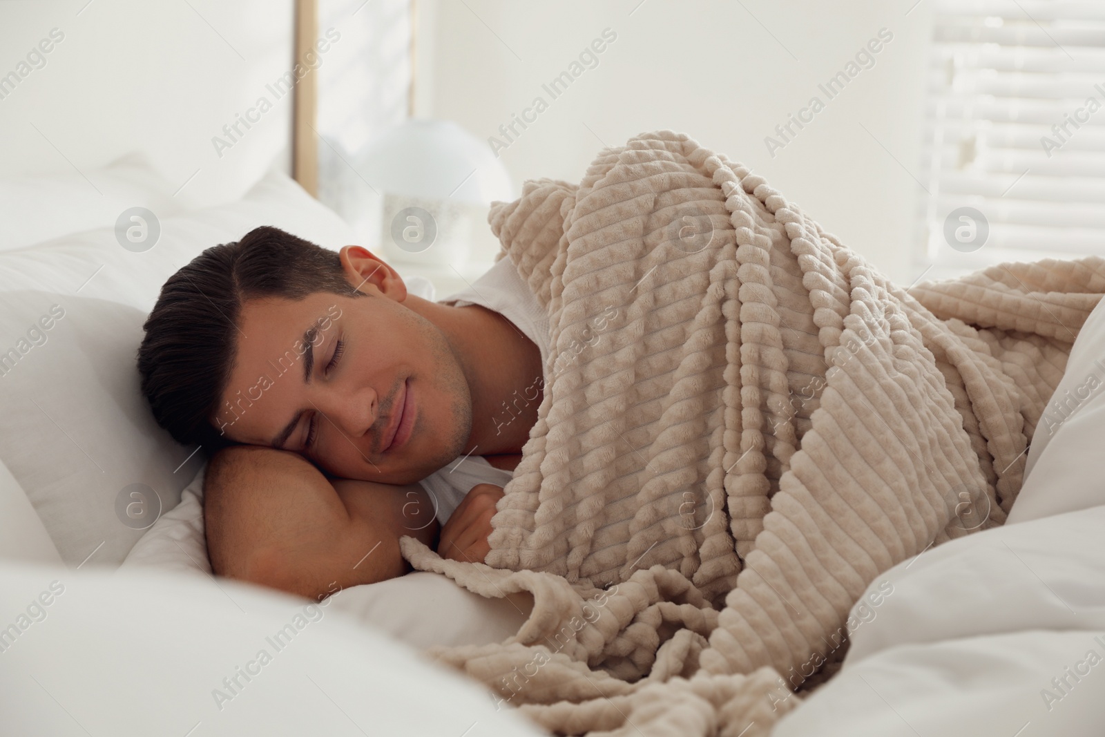 Photo of Man covered with warm beige plaid lying in bed indoors