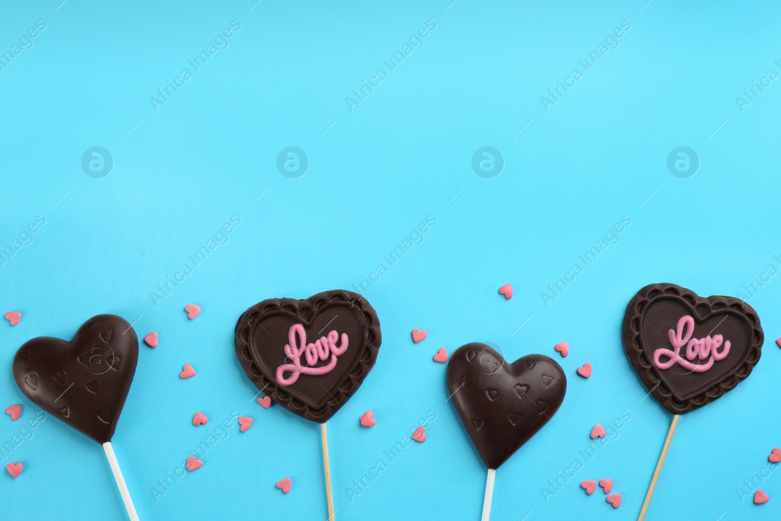 Photo of Different chocolate heart shaped lollipops and sprinkles on light blue background, flat lay. Space for text