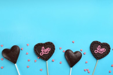 Different chocolate heart shaped lollipops and sprinkles on light blue background, flat lay. Space for text