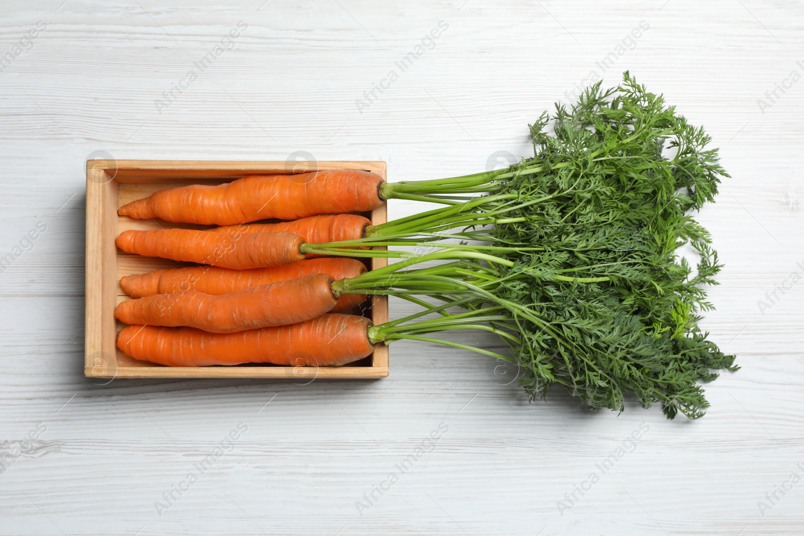 Photo of Fresh carrots in crate on white wooden table, top view