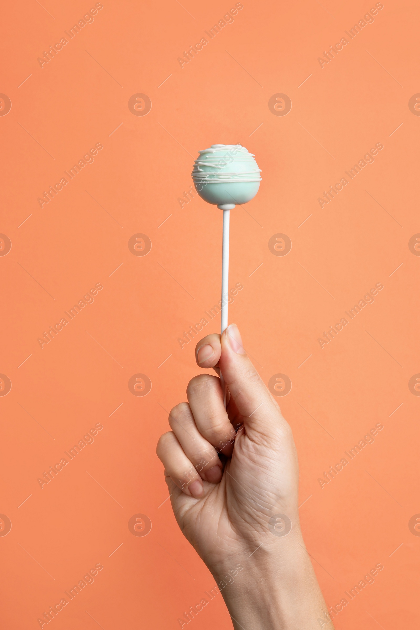 Photo of Woman holding sweet cake pop on coral background, closeup