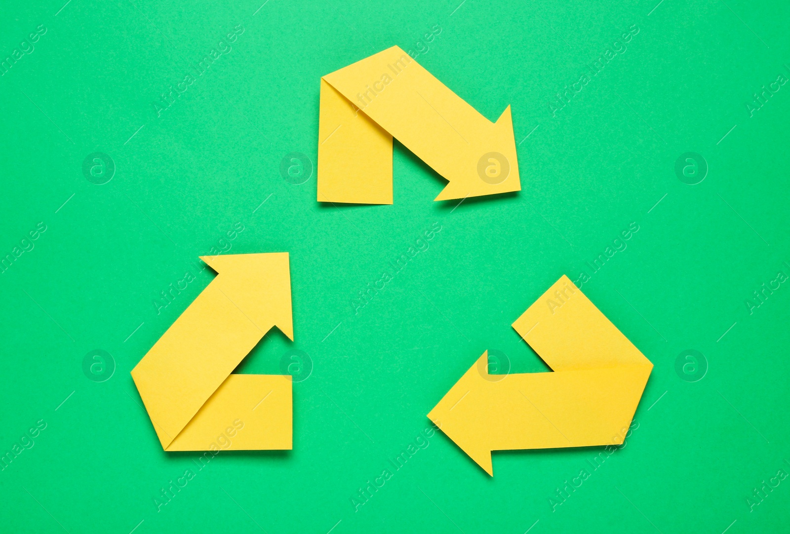 Photo of Recycling symbol made of yellow paper arrows on green background, top view